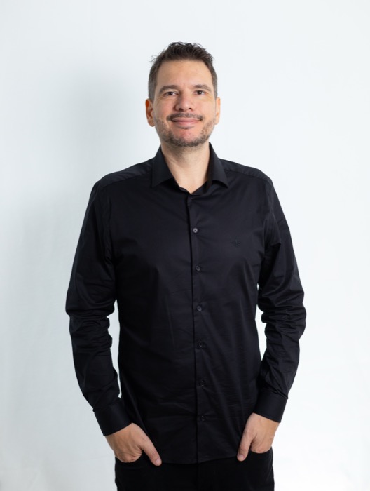 Fernando Palacios, de camisa preta, em pé diante de fundo branco.